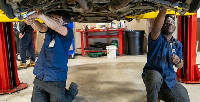 Two Porter and Chester Institute automotive students working beneath a vehicle on lifts