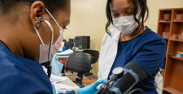 Two Porter and Chester Institute healthcare students in scrubs practicing a blood pressure reading