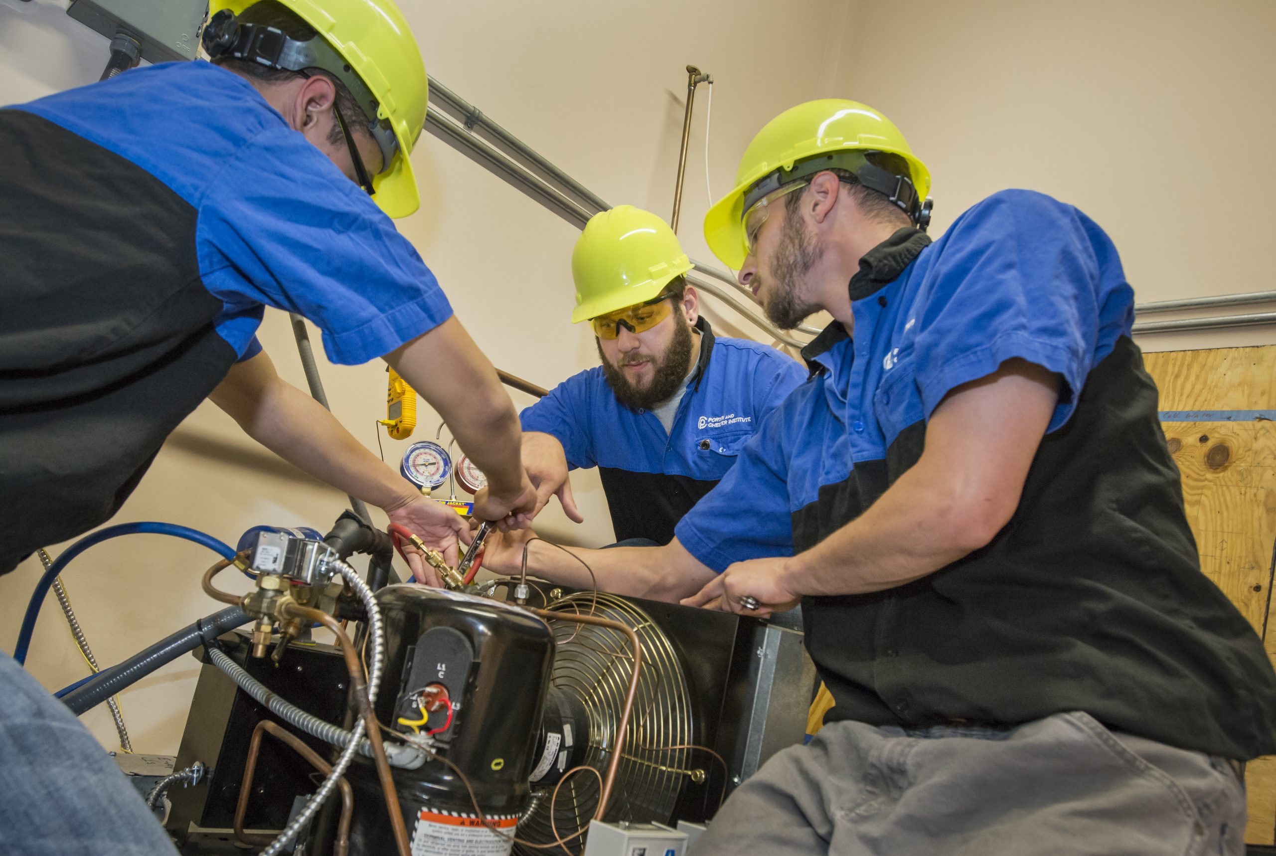 Porter and Chester Institute students in hard hats servicing HVAC refrigeration equipment during hands-on training